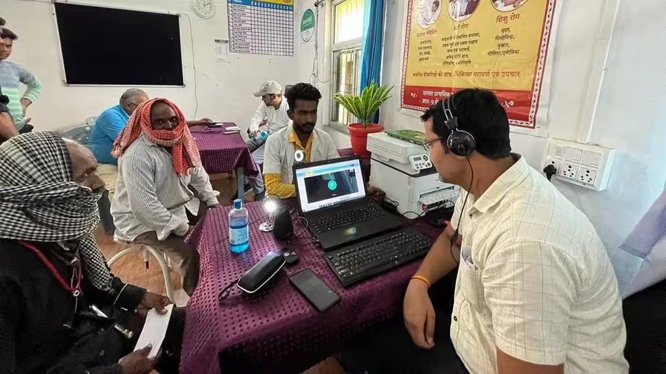 A teleconsultation at a health centre: a laptop showing a video call, a headset, and patients waiting around the table
